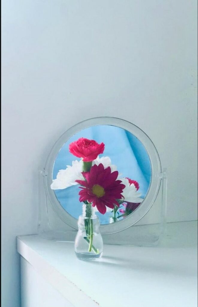 Petit miroir rond reflétant un bouquet de fleurs colorées, pour symboliser la découverte de son corps