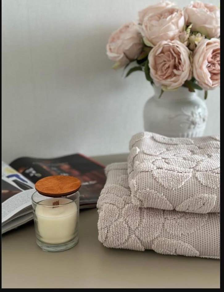 Bougie parfumée et serviettes moelleuses près d'un bouquet de roses pastel, ambiance cocooning pour un massage en couple