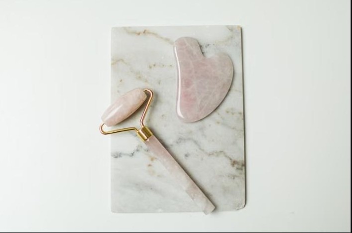 Rouleau de massage facial et pierre gua sha en quartz rose sur du marbre, symbole de bien-être et santé