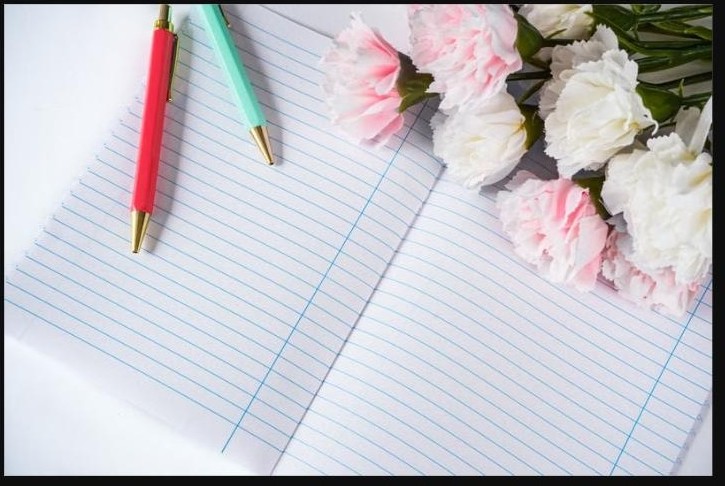 Carnet ouvert avec deux stylos colorés et un bouquet de fleurs, pour symboliser la parole libérée entre femmes