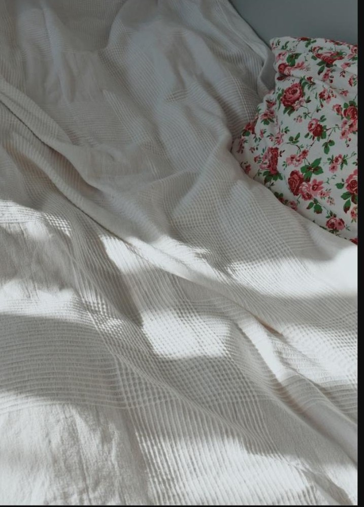 Draps froissés en lumière douce du matin avec un coussin fleuri, ambiance intime et paisible