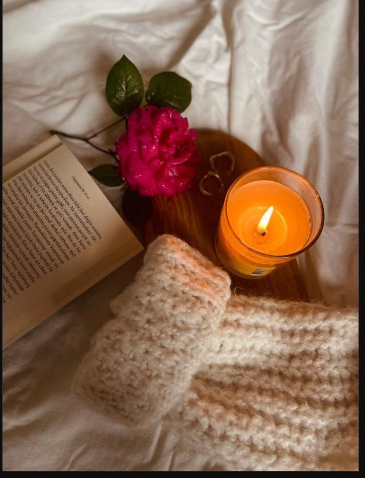 Livre, bougie allumée et pull douillet sur un lit, moment cocooning pour se retrouver après la maternité