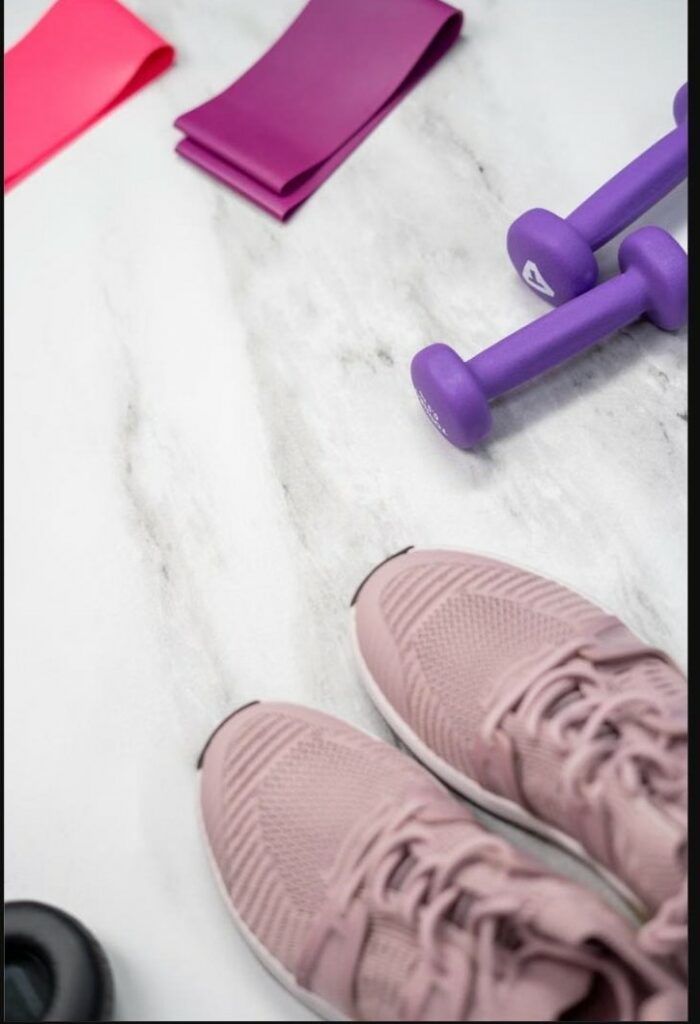Baskets roses, élastiques de fitness et haltères violets posés sur du marbre, symbole du lien entre sport et bien-être