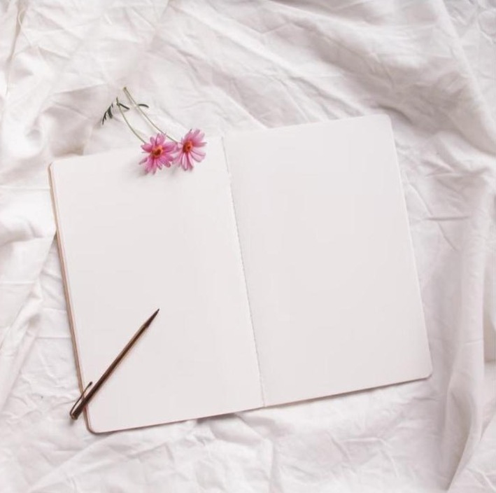 Carnet ouvert avec fleurs roses et stylo sur lin blanc, symbole de nouveau départ et de découverte en douceur