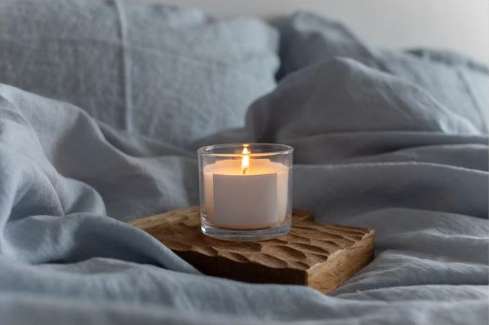 Bougie allumée posée sur du linge de lit doux, ambiance cocooning pour un rituel du soir