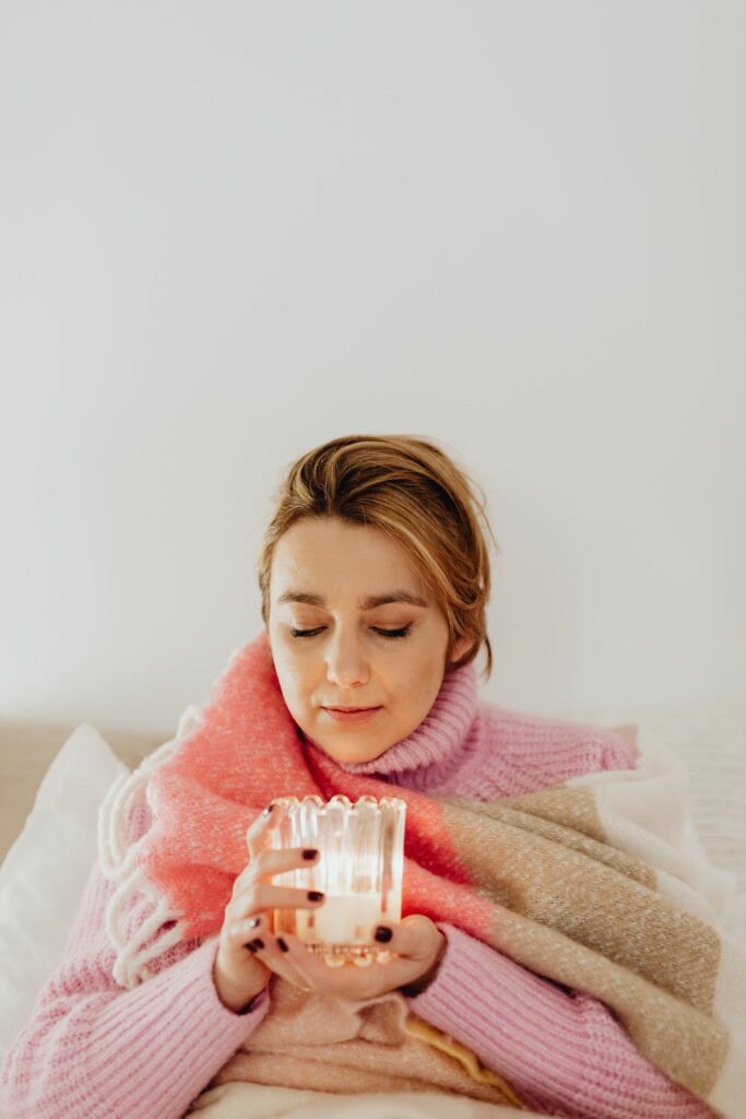 Femme enveloppée dans un plaid tenant une bougie, moment de calme et de reconnexion à soi