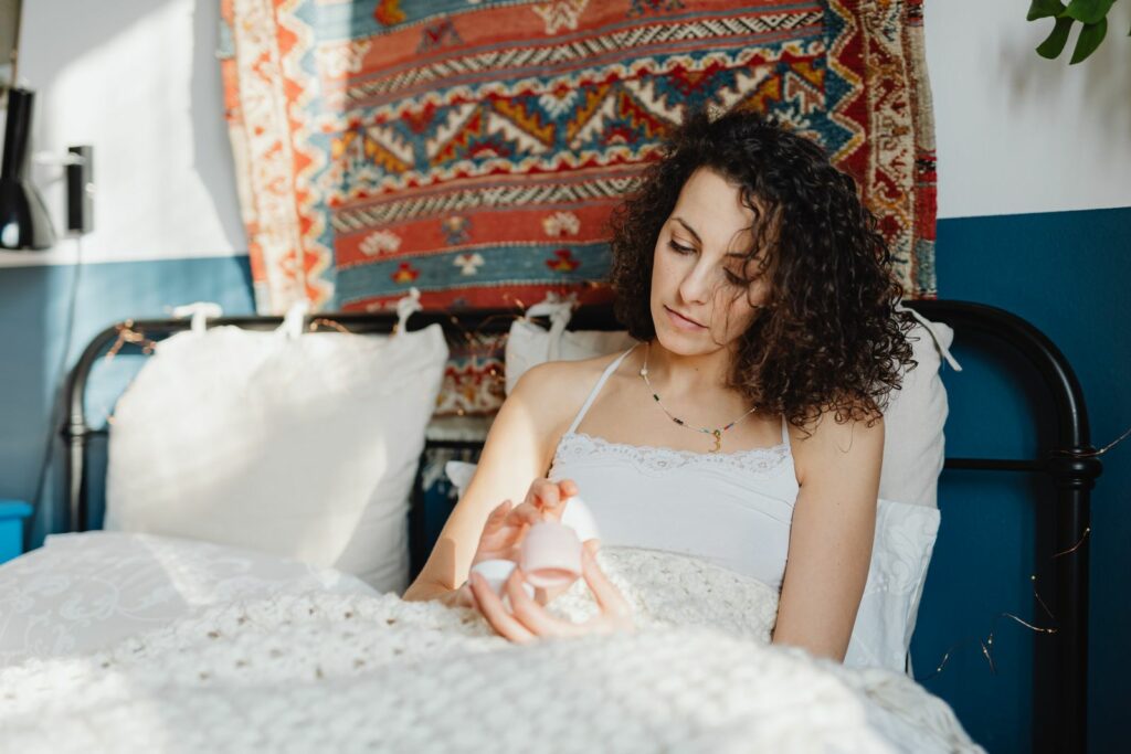 Femme assise sur son lit tenant un flacon de soin, moment de bien-être personnel - sécheresse intime