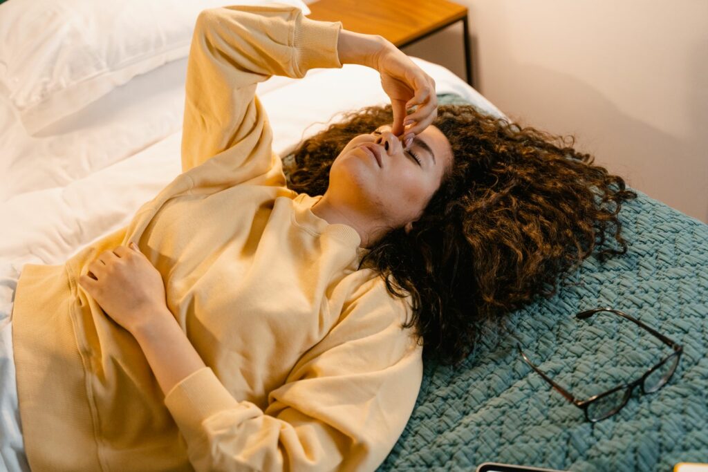 Jeune femme s'étirant dans son lit le matin, lumière chaude, fatigue post-partum